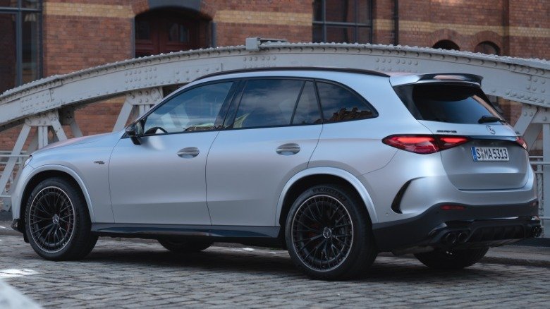 2027 Mercedes-AMG GLC53 Returns Six-Cylinder Power to Compact Performance SUV Lineup 2 A rear three-quarters shot of the matte silver AMG GLC53 SUV parked on a cobblestone bridge in front of a brick building