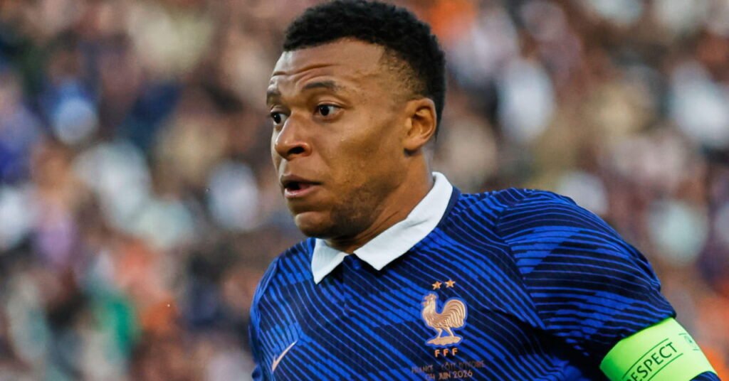Didier Deschamps Delivers Emotional Farewell Ahead of Final Match as France Manager 2 Footballer Kylian Mbappe playing for the France national football team at the World Cup 2026 while wearing a blue shirt with a golden logo on the chest and a white collar with a green captain's armband on his left arm while looking to his right with a crowd blurrily visible in the background