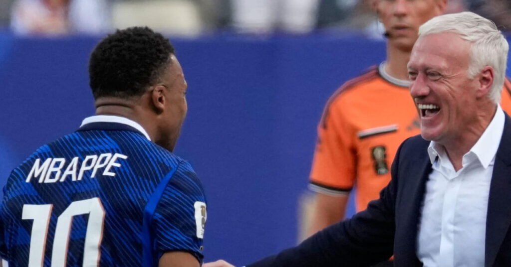 Didier Deschamps Delivers Emotional Farewell Ahead of Final Match as France Manager 5 Footballer Kylian Mbappe looking to his right and celebrating on a pitch while wearing a blue France national football team shirt with his name and number 10 on the back at the World Cup 2026, celebrating with head coach Didier Deschamps, who is smiling and wearing a dark suit jacket and white shirt