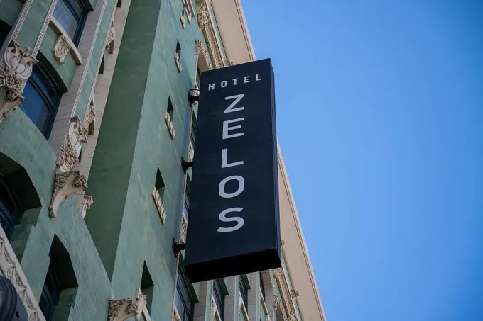 Vertical sign for Hotel Zelos on green tiled historic facade under clear blue sky, San Francisco, California, August 19, 2025.