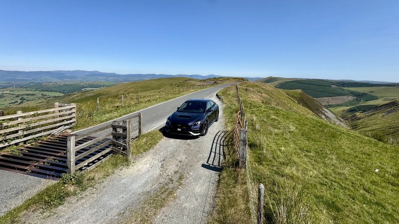 2026 Subaru WRX Base First Drive: Performance Value Purified 7 An overhead shot of a Galaxy Purple Pearl WRX parked on a gravel turnout next to a cowcatcher on the peak of a grassy mountain with a view of meadows and blue skies