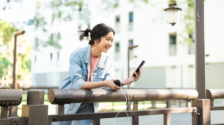 Why Using Your Phone While Charging Won't Ruin Its Battery — The Science of Power Management 2 A woman leaning against a railing and enjoying a video call on a phone while it's plugged into a charger.