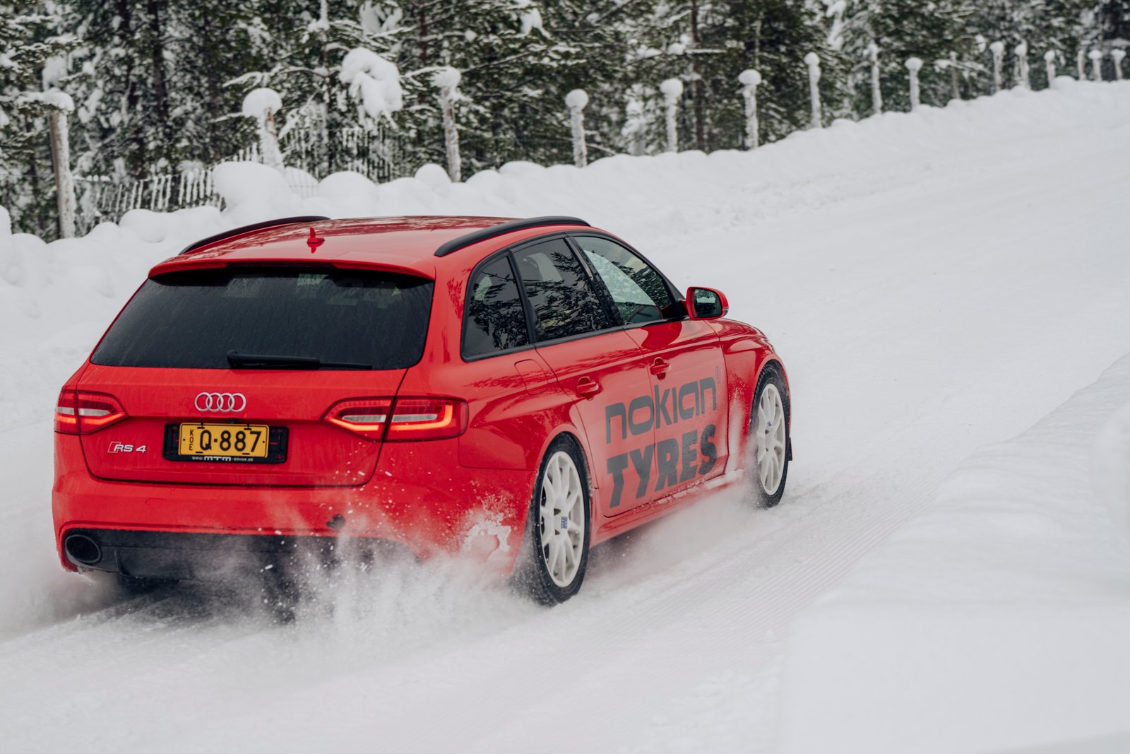 A red audi station wagon drives on ice, away from the camera