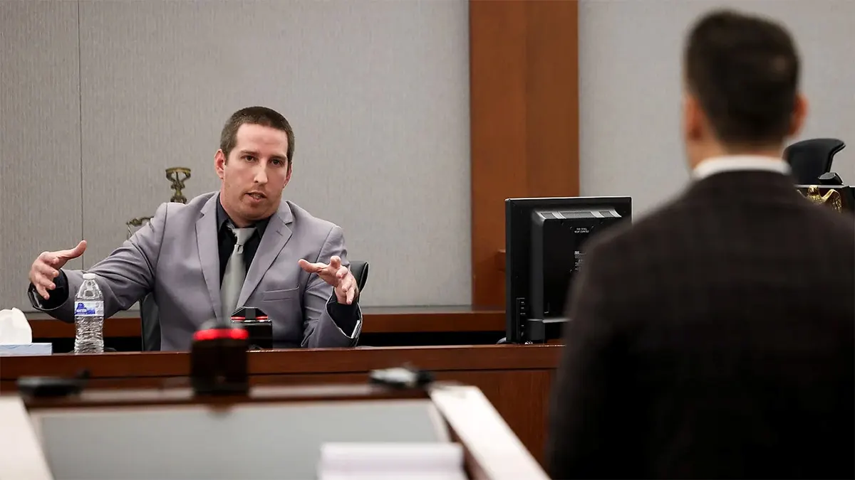 Mitchell Fairbarn, wearing a gray suit and tie, gestures with both hands while testifying in a Las Vegas courtroom.