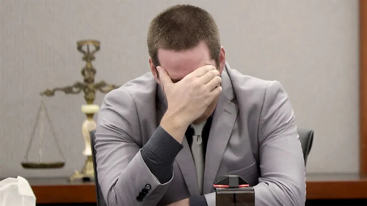 Mitchell Fairbarn sits in a Las Vegas courtroom wearing a gray suit, leaning forward with one hand covering his face.