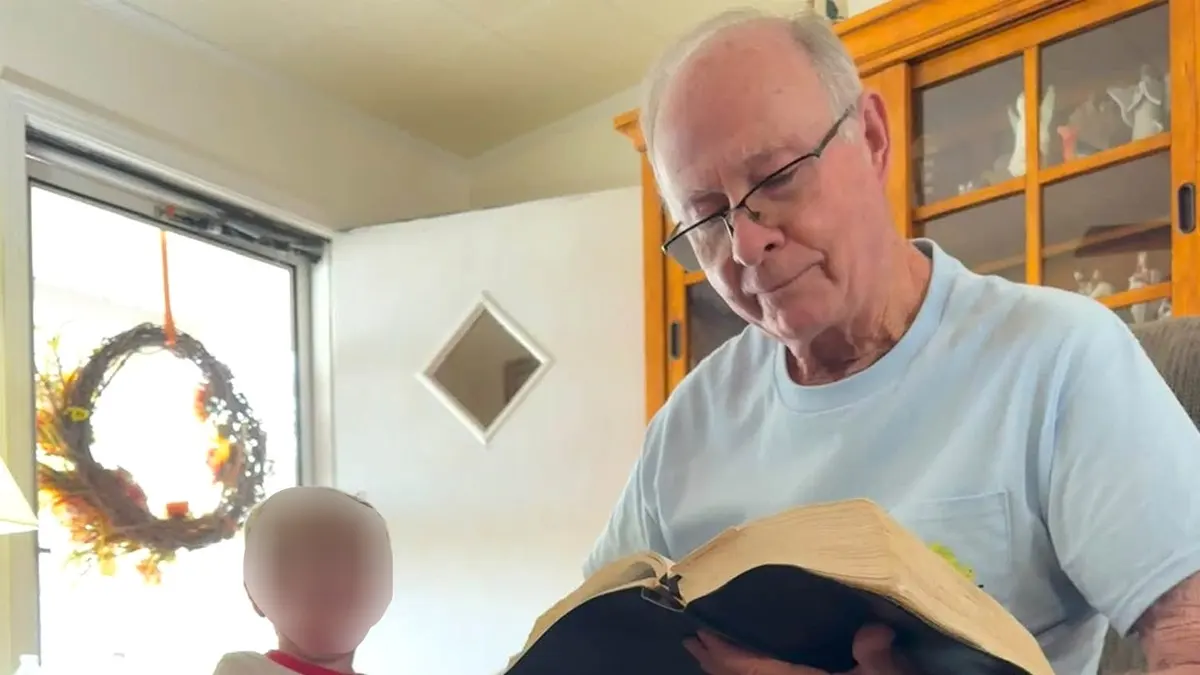 Bobby McGill, wearing glasses and a light blue shirt, reads an open Bible while seated beside a young child.
