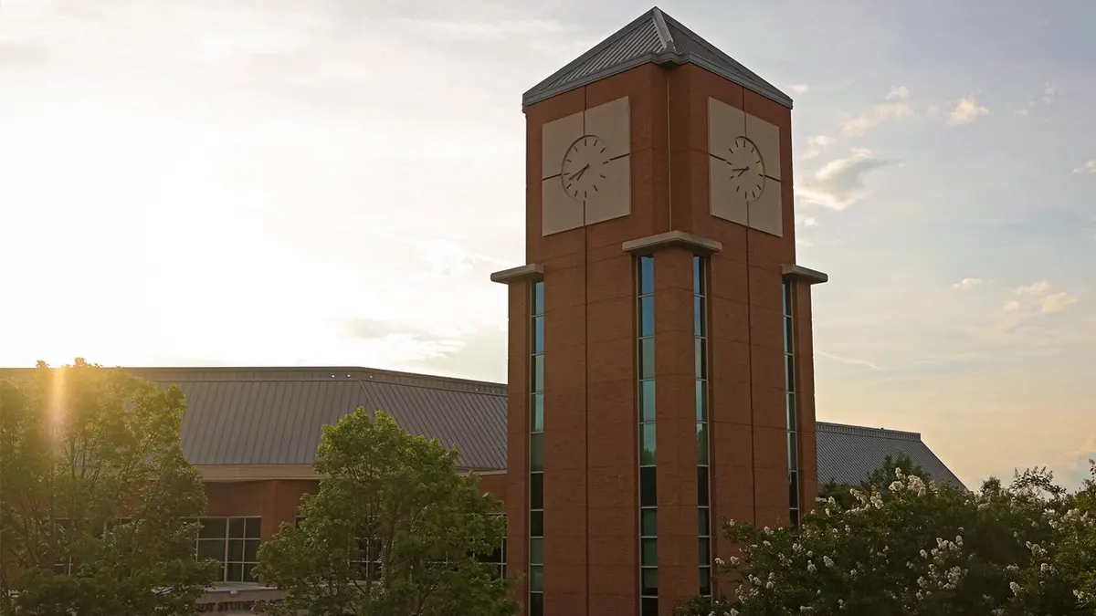 A tall brick clock tower rises above trees and campus buildings at the University of North Carolina at Charlotte.