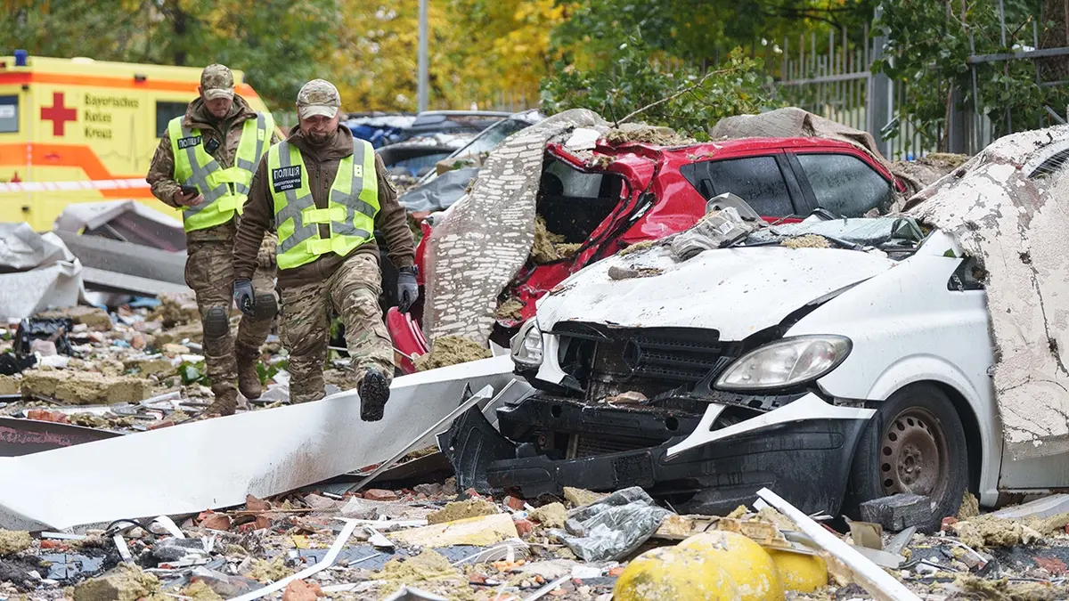 Policemen walk in front of destroyed cars in a damaged residential building yard in Kyiv.